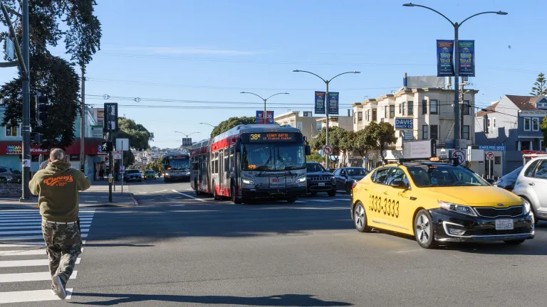 A pedestrian in a crosswalk, a taxi, and a Muni bus at an intersection in San Francisco.