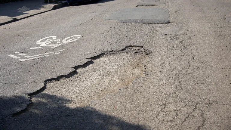 Potholes in the pavement next to a sharrow bike marking.