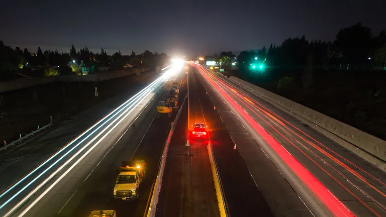 A long-exposure photo shows cars streaking down the highway at night.