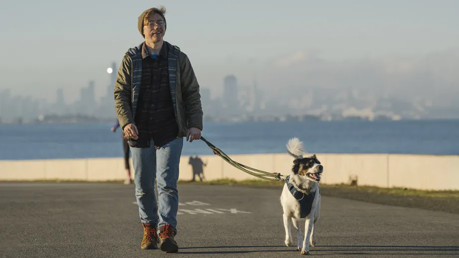 A person walking their dog, with the San Francisco skyline behind.
