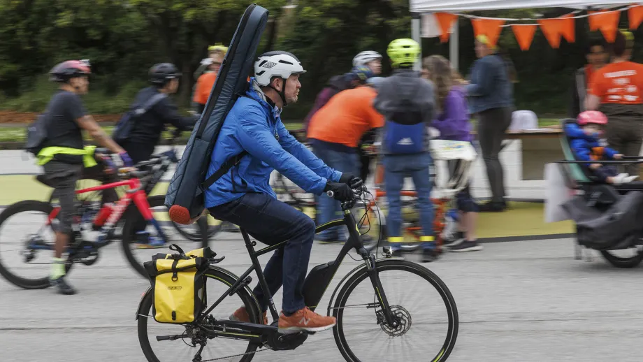 A cyclist with panniers and a guitar riding past the Bike to Work Day Energizer Station in San Francisco's Golden Gate Park.