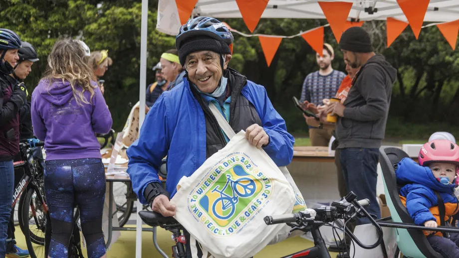 A senior cyclist proudly holds a 30th Anniversary Bike to Work Day tote bag.