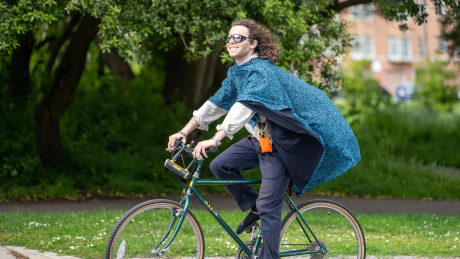 A person in a cape smiling as they bike through Golden Gate Park.