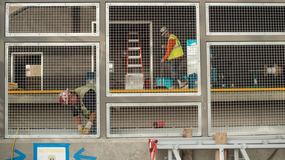Warm Springs BART Station: One worker screws in a screen, while the other worker sweeps the top of the platform.