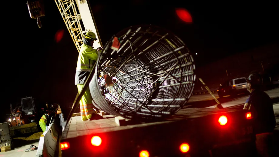 Construction crews unload a pre-fabricated metal rebar cage. This cage reinforces the foundations once concrete is poured.