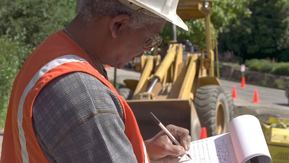 A construction site manager writes on a clipboard at an MTC-funded project.