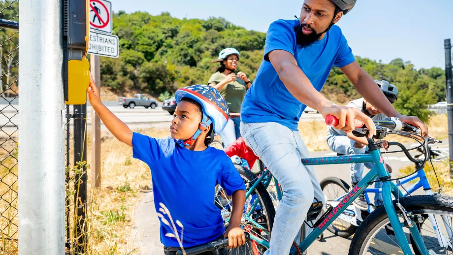 A cycling family presses the crosswalk button on their route.