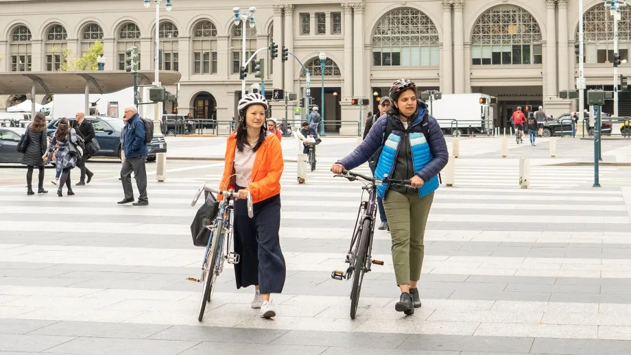 Two people walking their bicycles across a pedestrian plaza.