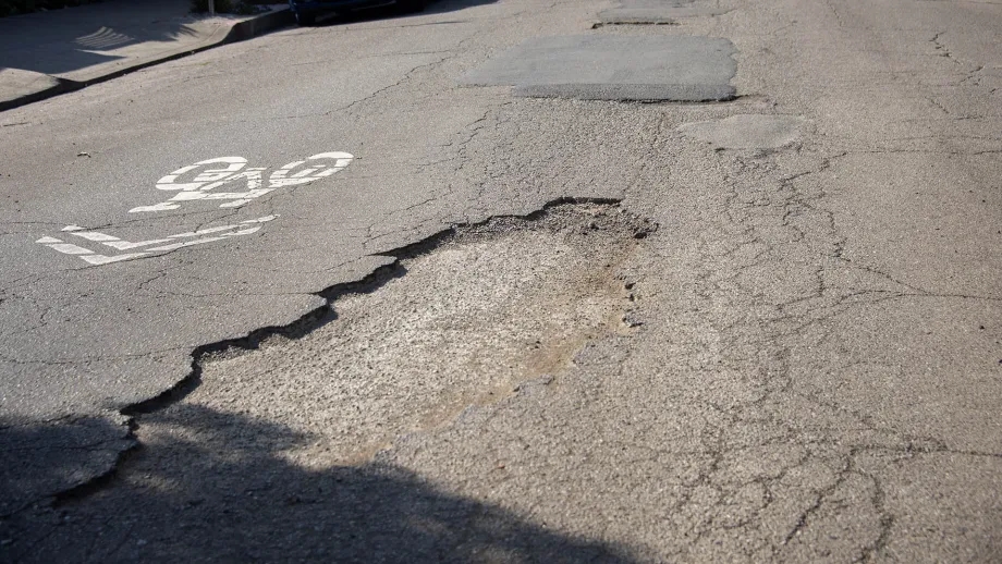 Potholes in the pavement next to a sharrow bike marking.