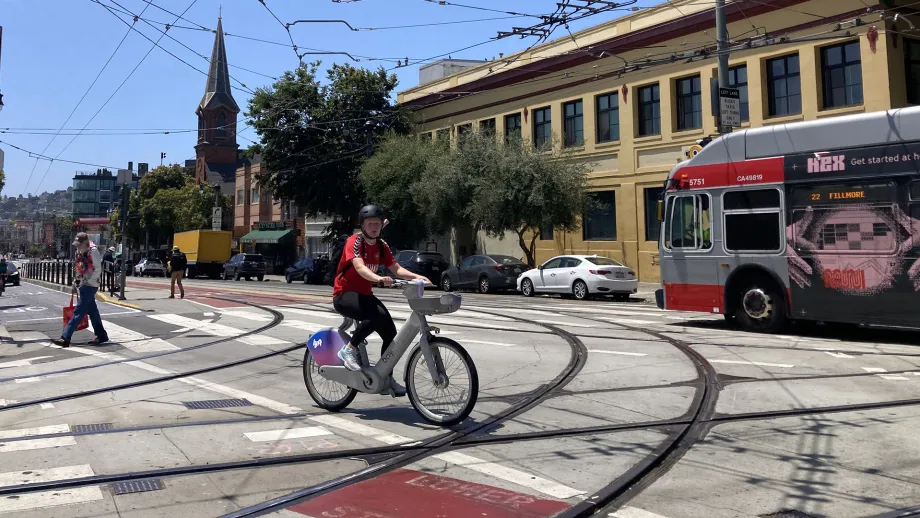 A San Francisco Bay Wheels rider crossing Muni light rail tracks as a bus passes.