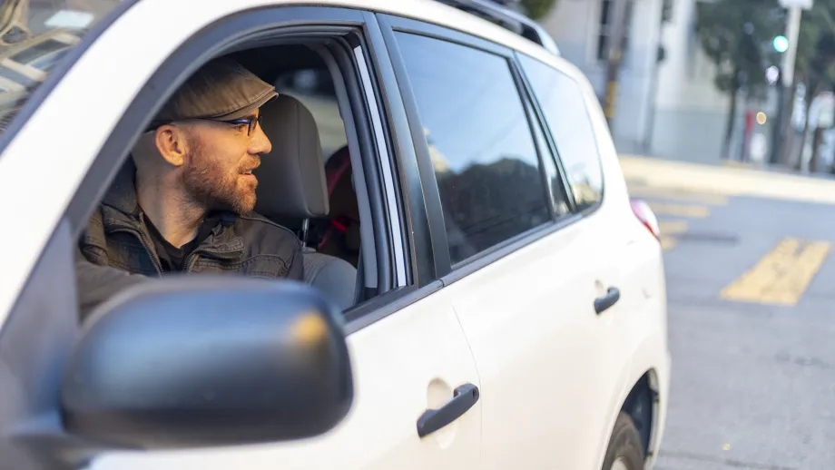 A driver using the Dutch Reach technique to open his car door while prioritizing the safety of passing cyclists.