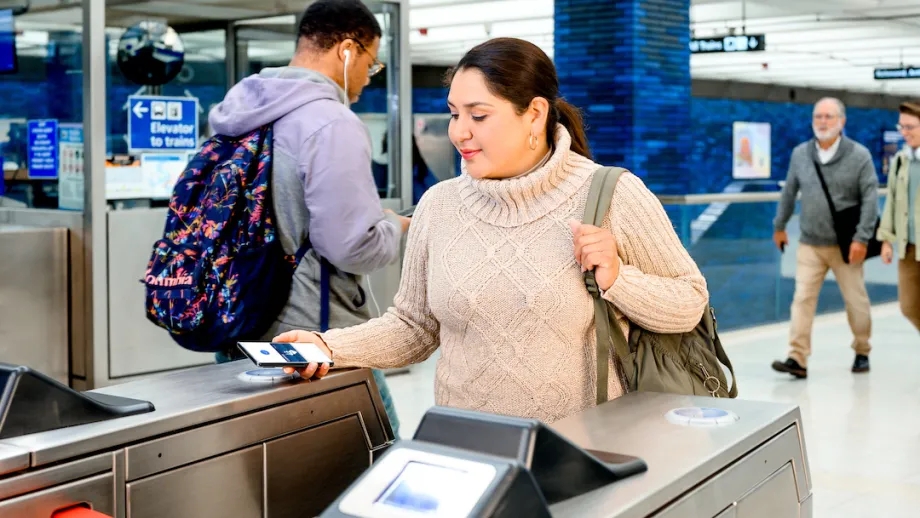 Woman taps phone with Clipper app open on BART turnstile in Oakland.