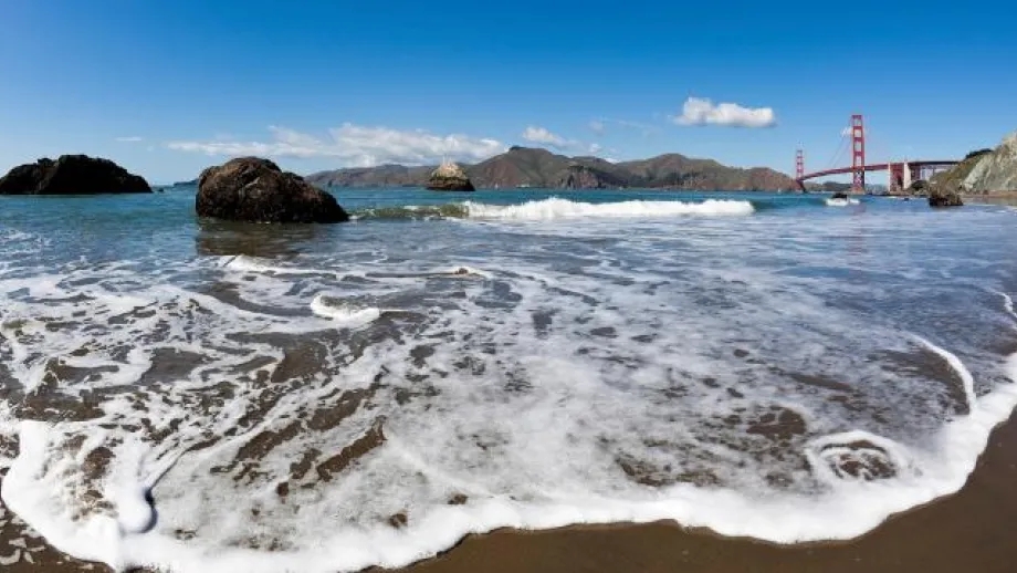 Waves lap up on shore with the Golden Gate Bridge in the distance